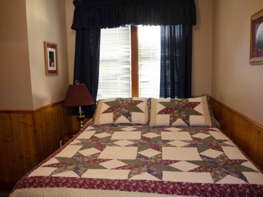 Een slaapkamer met een groot bed, een nachtkastje, een lamp en een raam met gordijnen.
