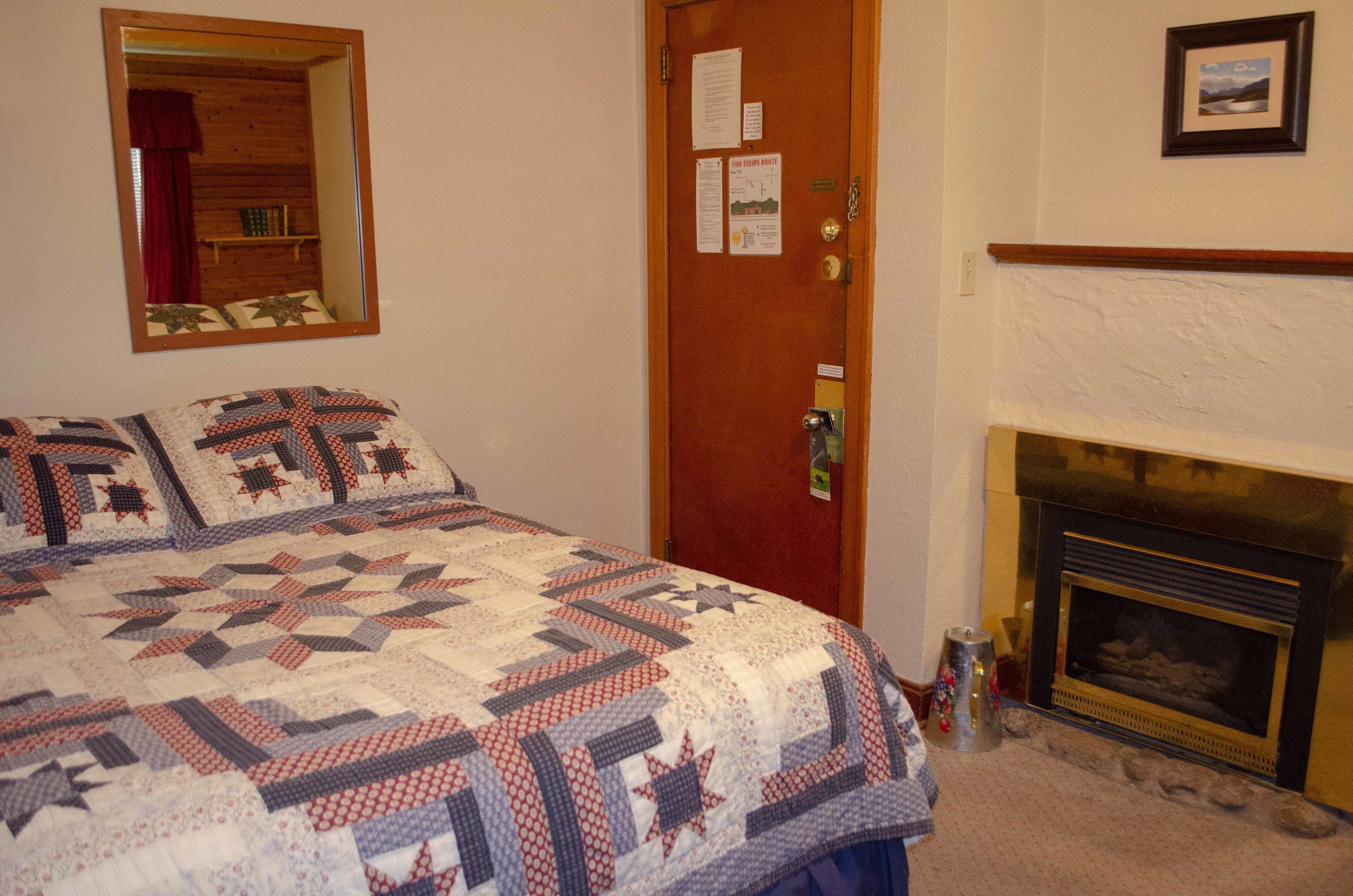 Een slaapkamer met een houten deur, een gewatteerde spreideken, een open haard en een spiegel aan de muur.