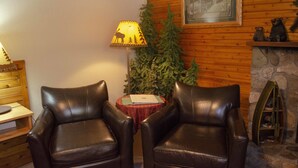 Een kamer met twee leren fauteuils, een tafel met een rode tafelkleed, een lamp met een silhouet van een hert, een kerstboom en een ingelijst beeld aan de muur.