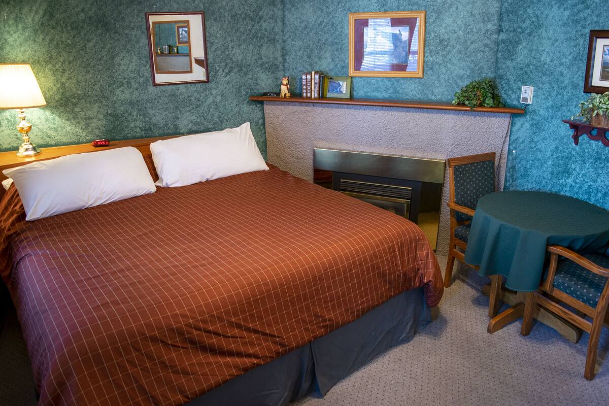 A hotel room with a large bed, a small table, and a fireplace.