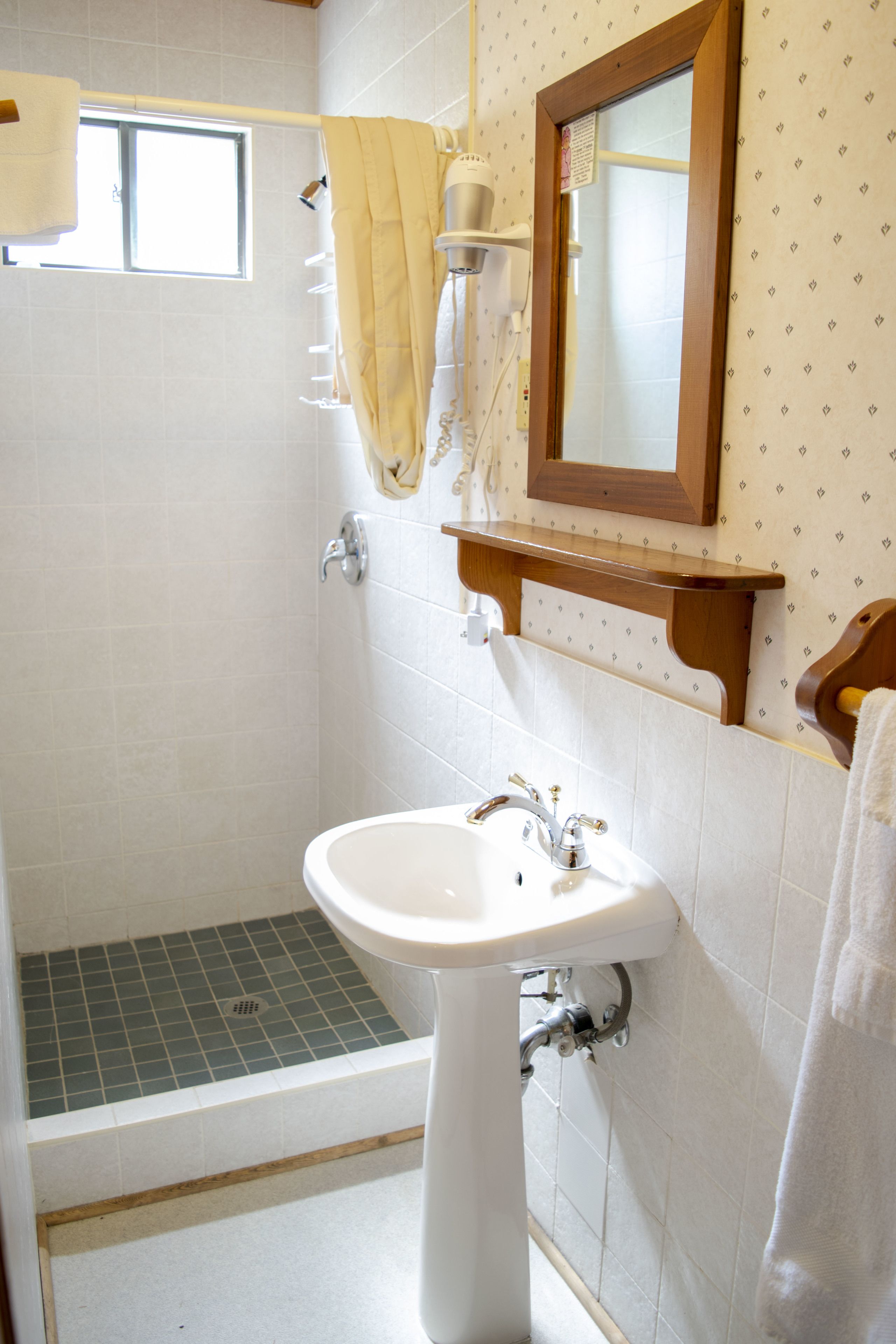 A bathroom with a white sink, a mirror, a shower, and a towel rack.