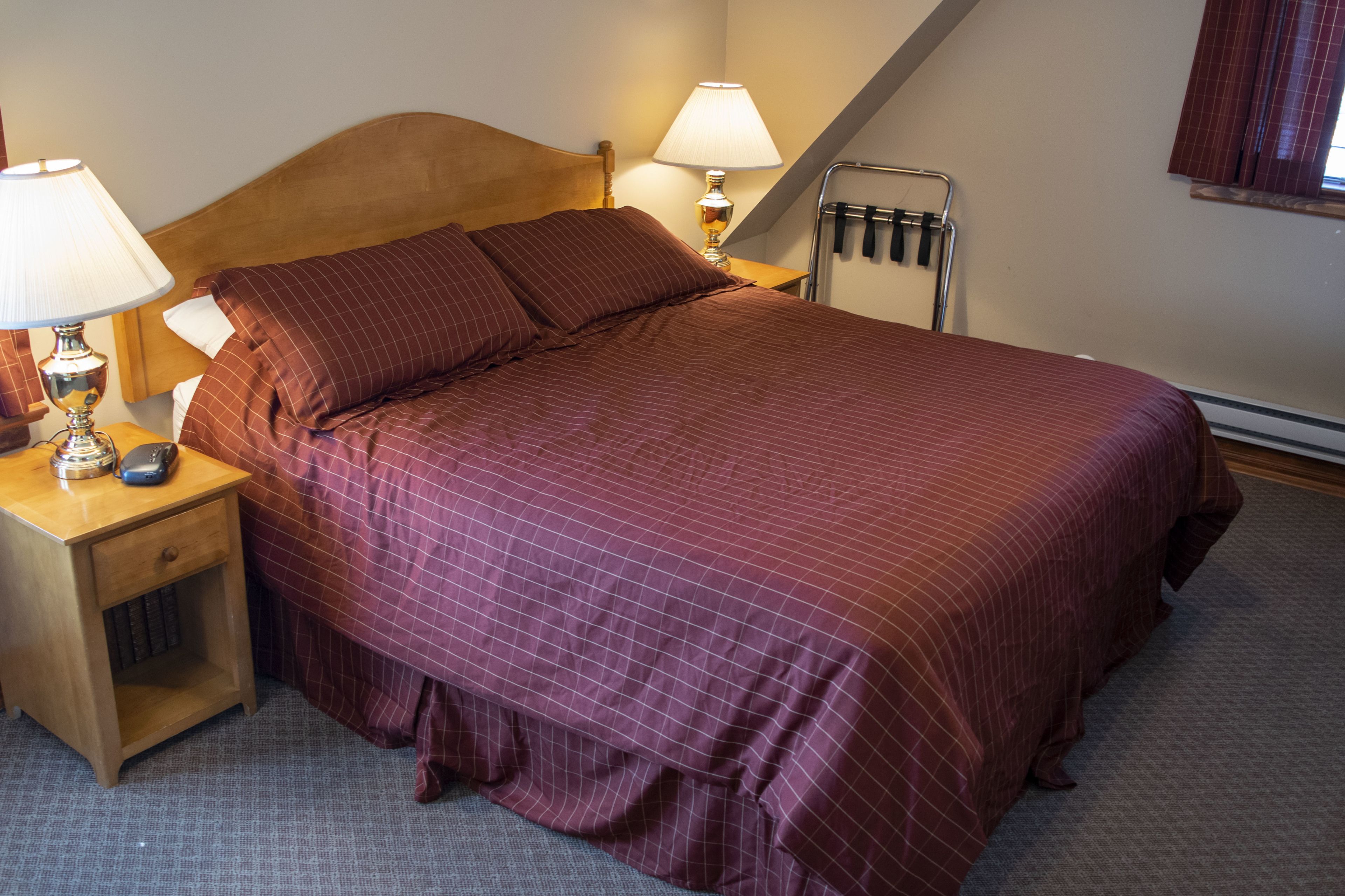 A neatly made bed with a wooden headboard, two bedside lamps, and a nightstand with a lamp and a phone.