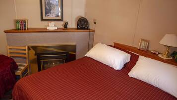 A hotel room with a large bed, a desk with a chair, a small table with a lamp, and a framed picture on the wall.