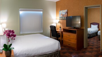 A hotel room with a large bed, a desk with a chair, a television, and a potted orchid.