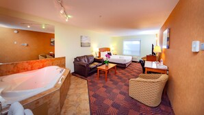 Una habitación de hotel con una bañera grande, un sofá, una mesita con una lámpara y una silla.