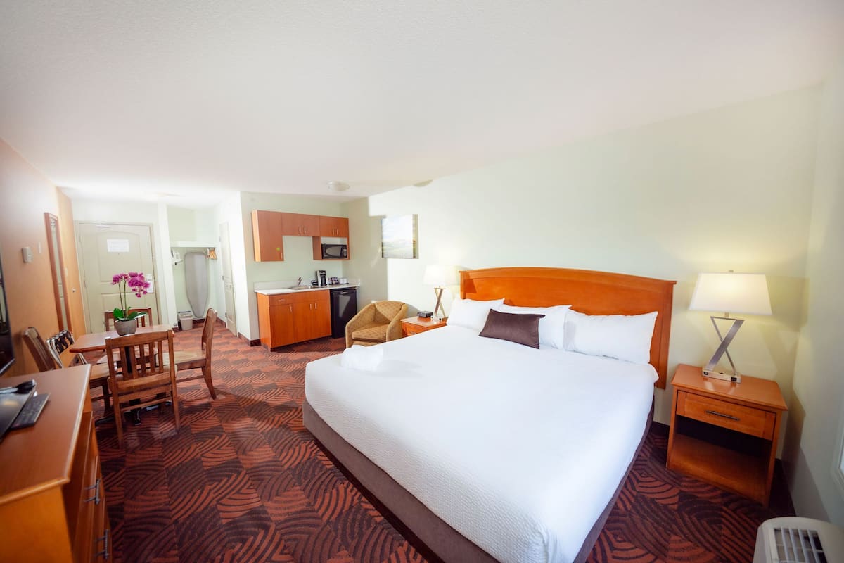 A hotel room with a large bed, a desk, a chair, a small kitchenette, and a bathroom.