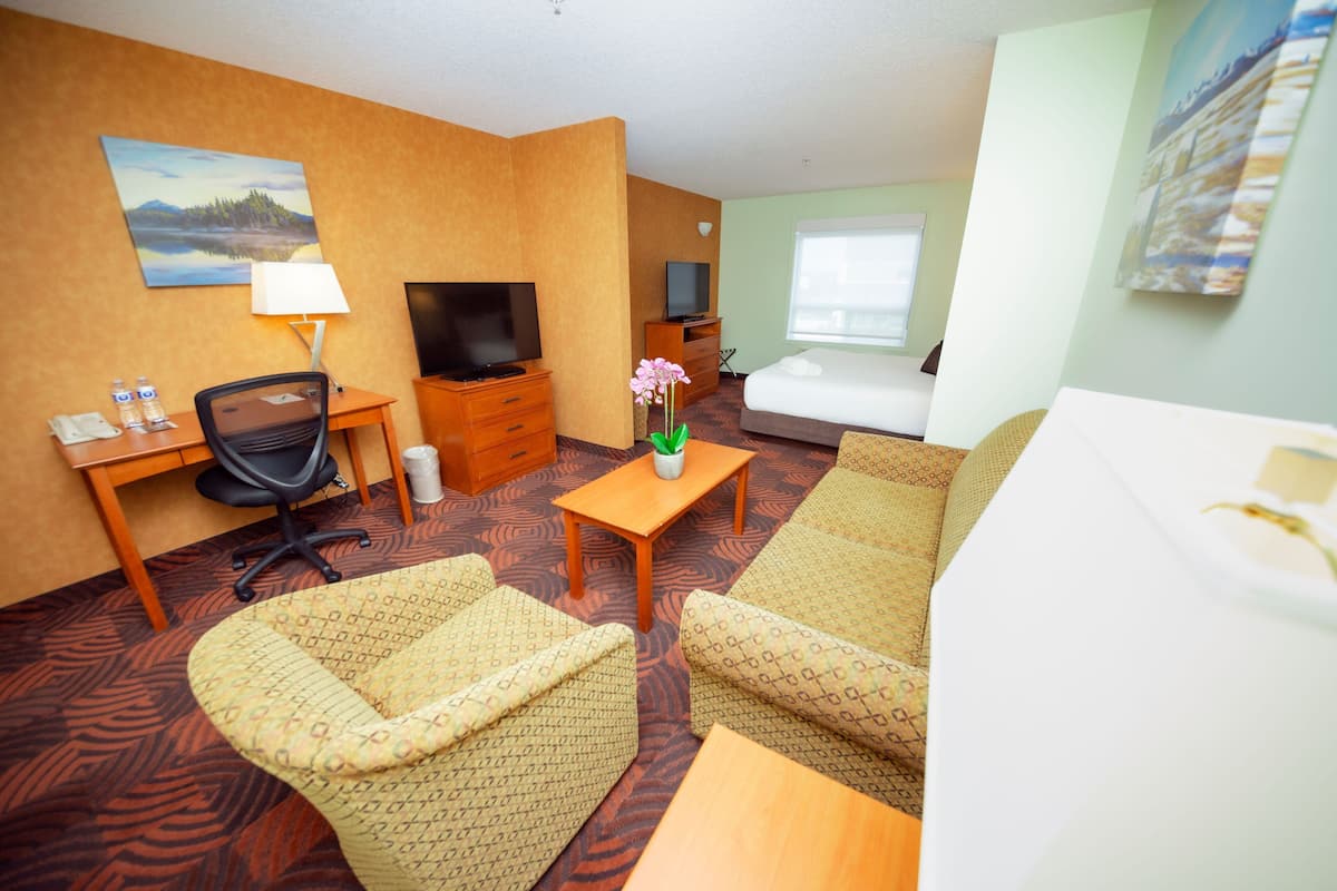 A hotel room with a bed, a desk with a chair, a television, a small table with a vase, and a painting on the wall.