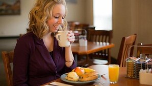 Una persona sentada a una mesa con un plato de comida, un vaso de jugo de naranja y una taza.