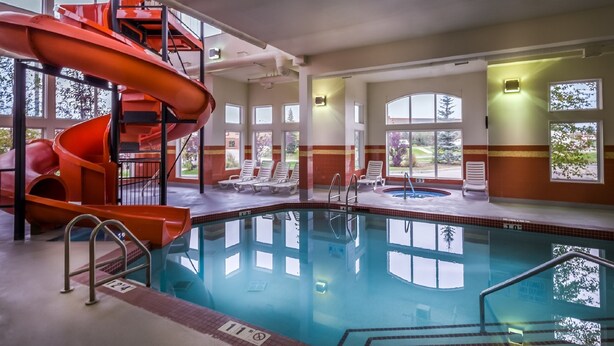 Una piscina interior con un tobogán espiral rojo, sillas de descanso y ventanas amplias.