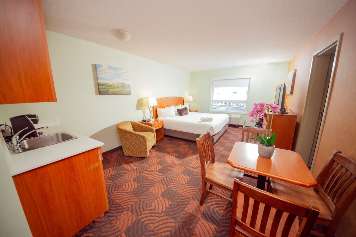 Une chambre d’hôtel avec un lit, un bureau, une chaise, une petite table, un lavabo et une fenêtre.