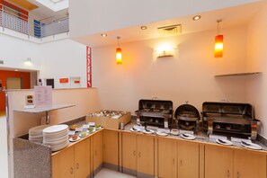 A buffet setup with multiple food stations, a counter with plates and cutlery, and a visible menu sign. - Ginger Vadodara (Vadodara)