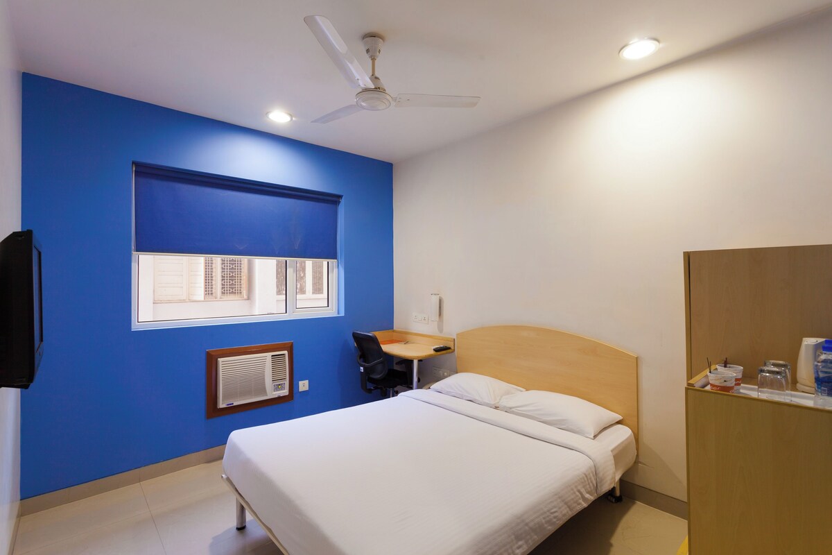 Une chambre à coucher comprenant un lit, un bureau, une chaise, une fenêtre, un ventilateur de plafond et une armoire.