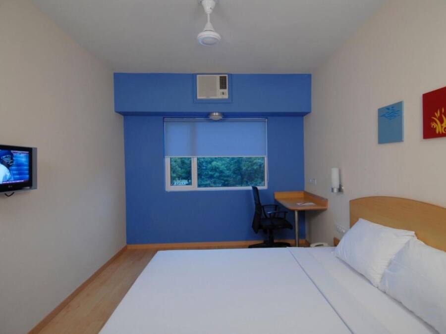 Una habitación de hotel con una cama, un escritorio, una silla, un televisor y una ventana.