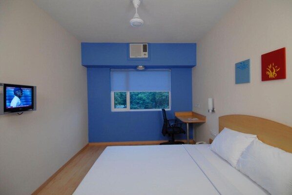 A hotel room with a bed, a desk, a chair, a television, and a window. - Ginger Vadodara (Vadodara)