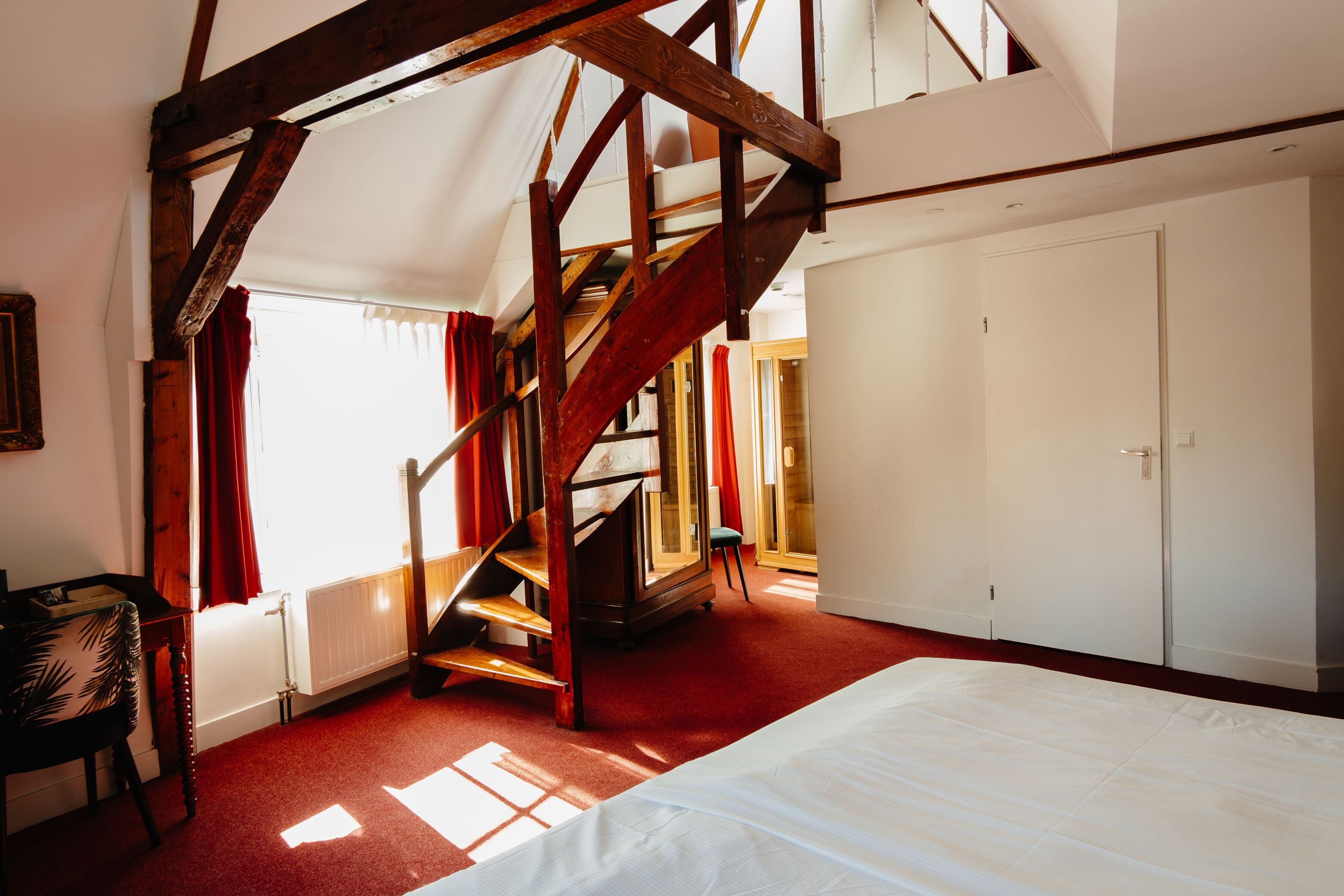 A bedroom with a large bed, a wooden staircase, and a wardrobe.