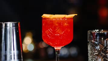 A bar setting with a cocktail glass, a shaker, and a glass on a bar mat.