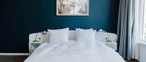 A neatly made bed with white bedding in a room with a dark teal wall.