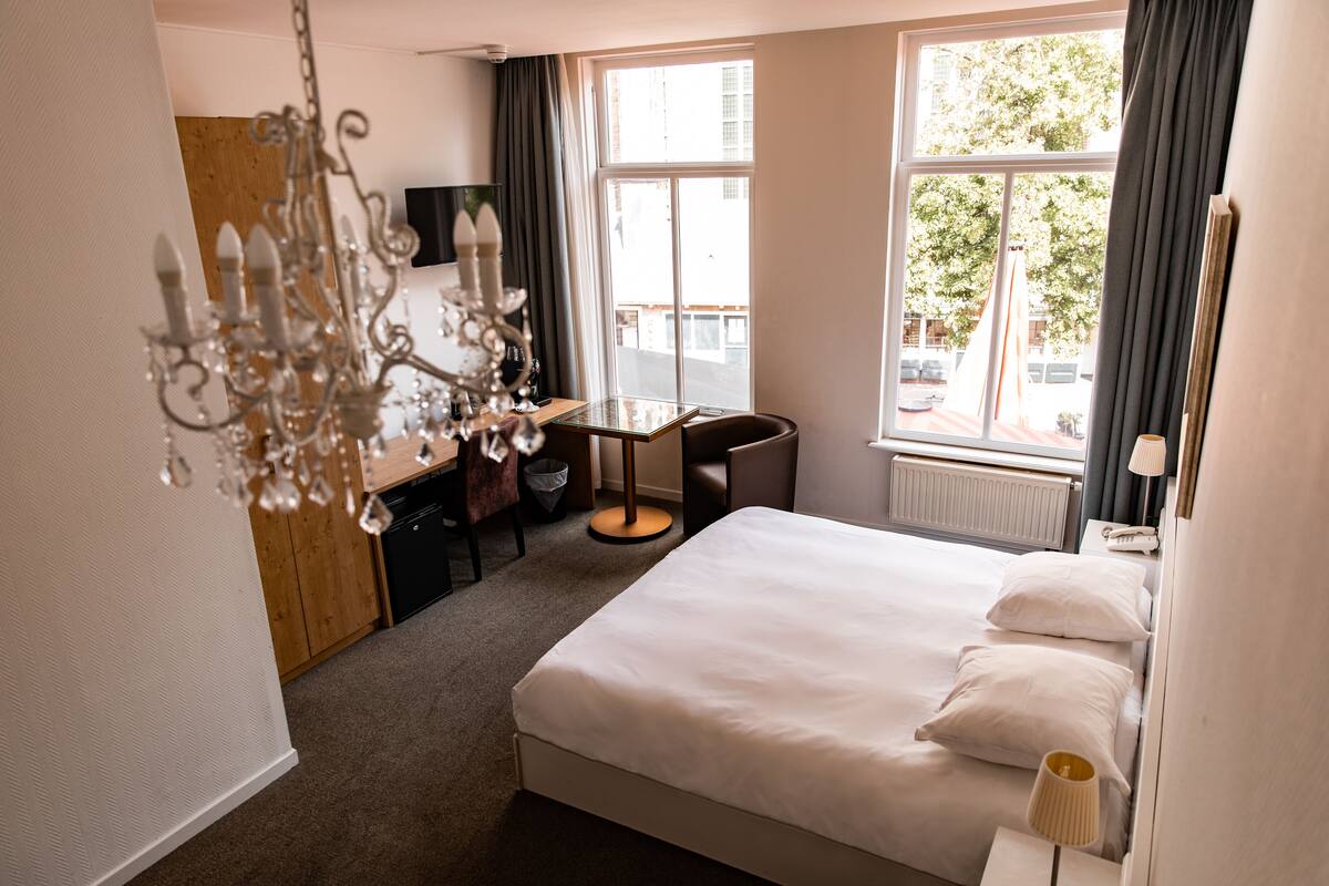 A hotel room with a bed, desk, chair, and a chandelier.