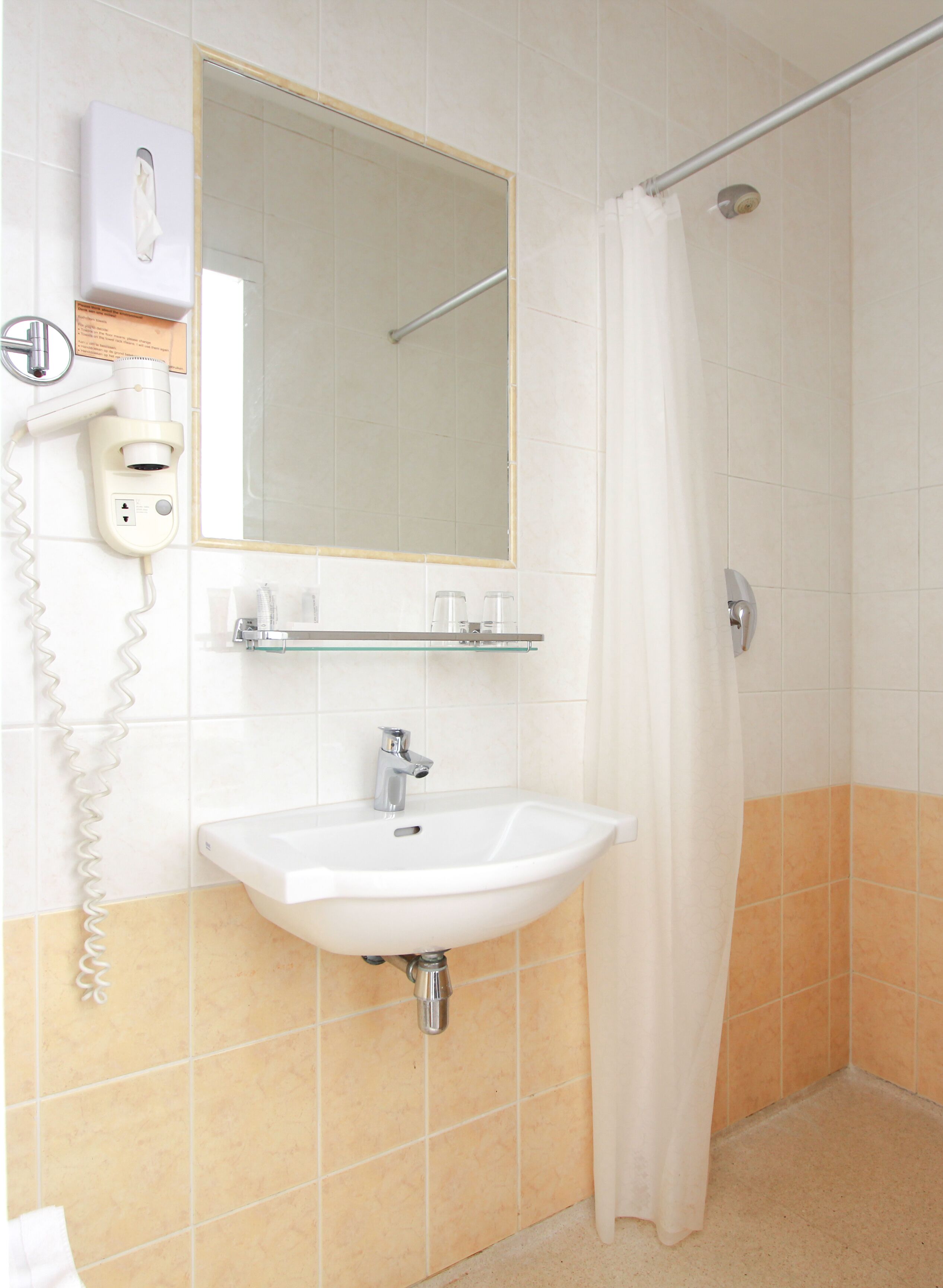A bathroom with a white sink, a mirror, a towel dispenser, and a shower curtain.