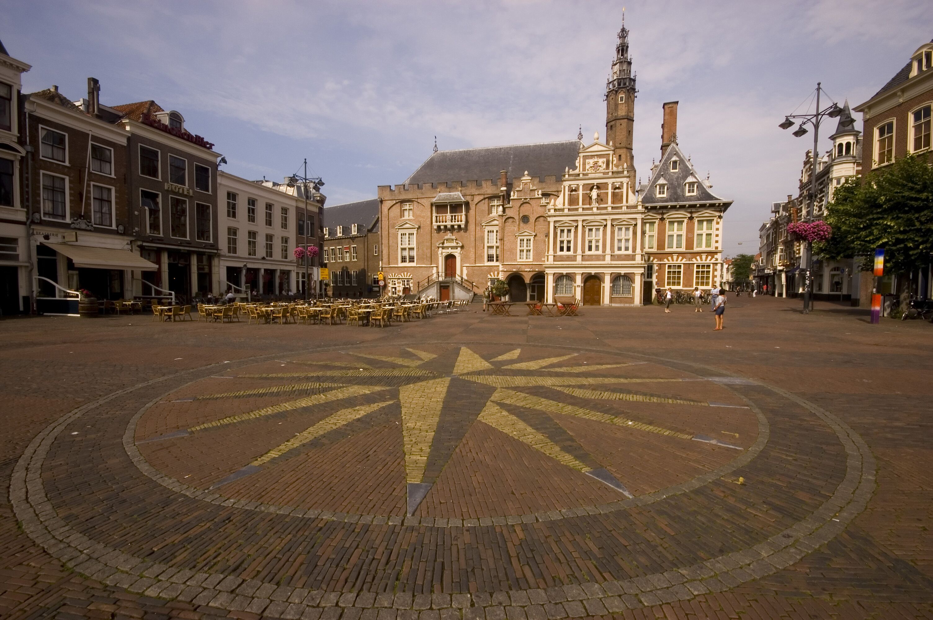 Una plaza histórica con un edificio destacado que tiene una torre del reloj, pavimento circular central y arquitectura tradicional circundante.