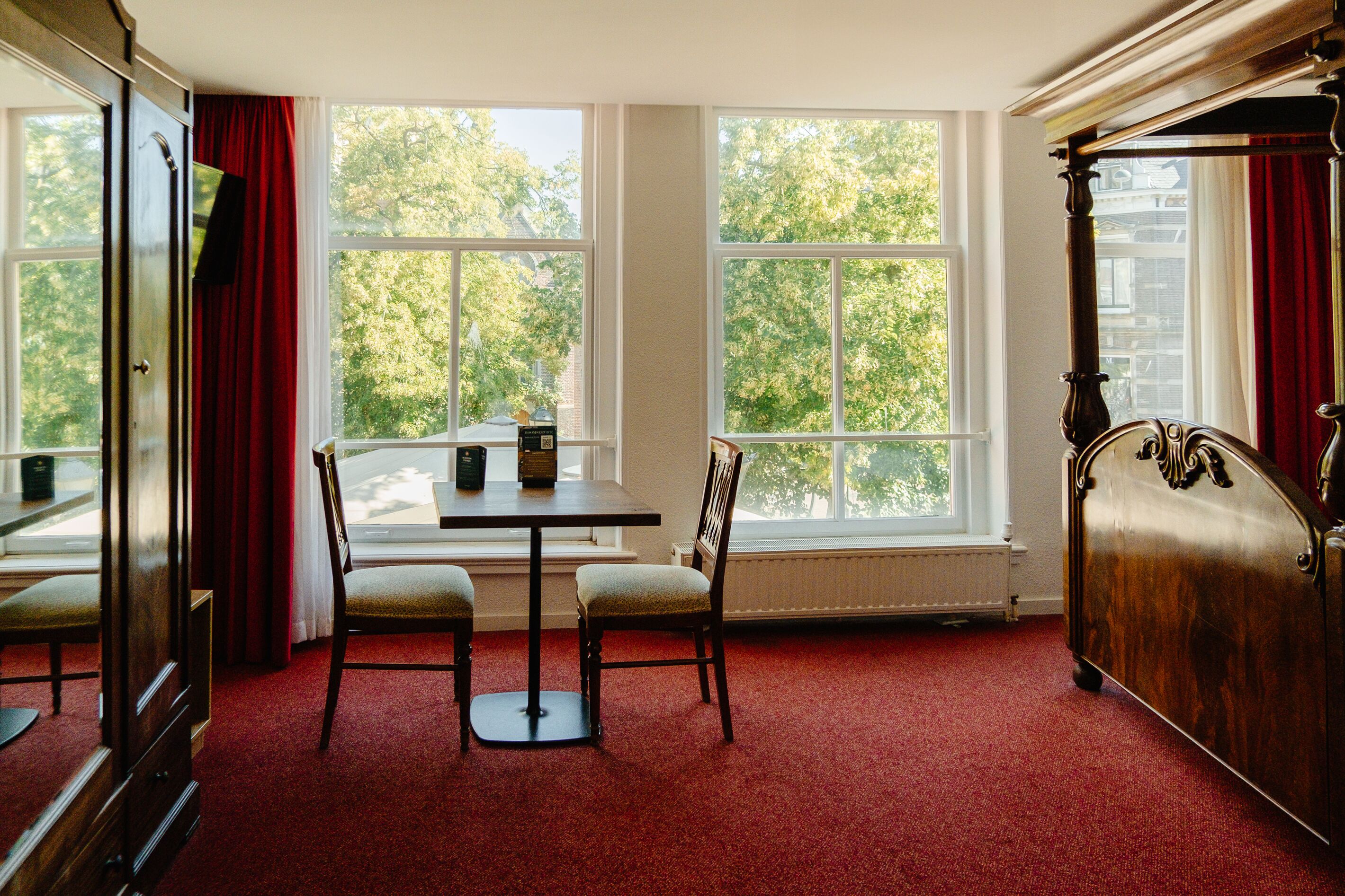 Una habitación con un gran ventanal, una mesa con dos sillas y una cama de madera.