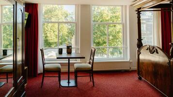A room with a large window, a table with two chairs, and a wooden bed.