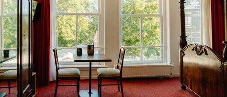 A room with a large window, a table with two chairs, and a wooden bed.