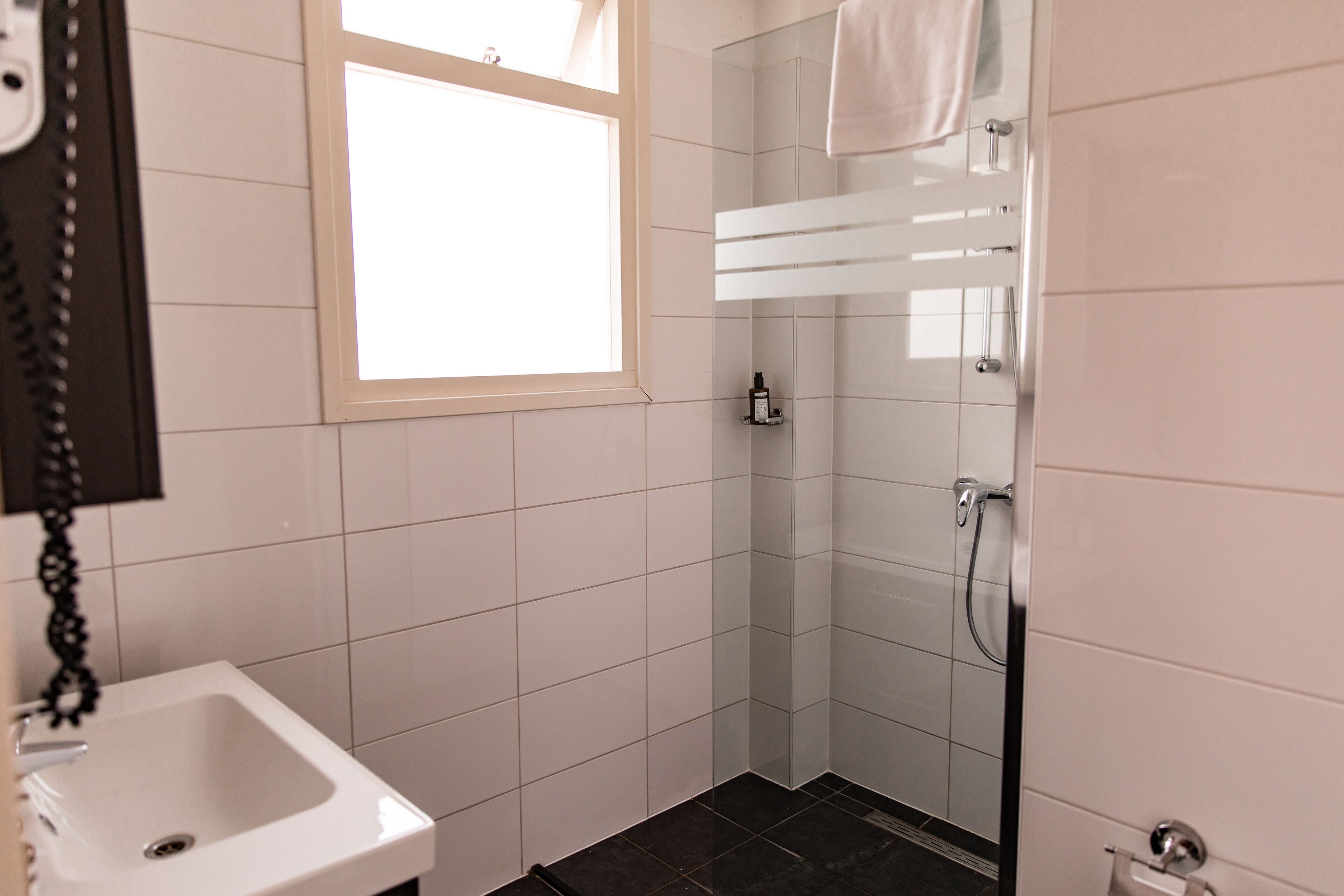 Ein Badezimmer mit einem weißen Waschbecken, einer Duschkabine aus Glas und einem Fenster.