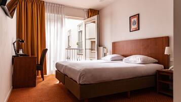 Habitación de hotel con cama, escritorio, silla, mesita de noche, ventilador de techo y ventana con cortinas.