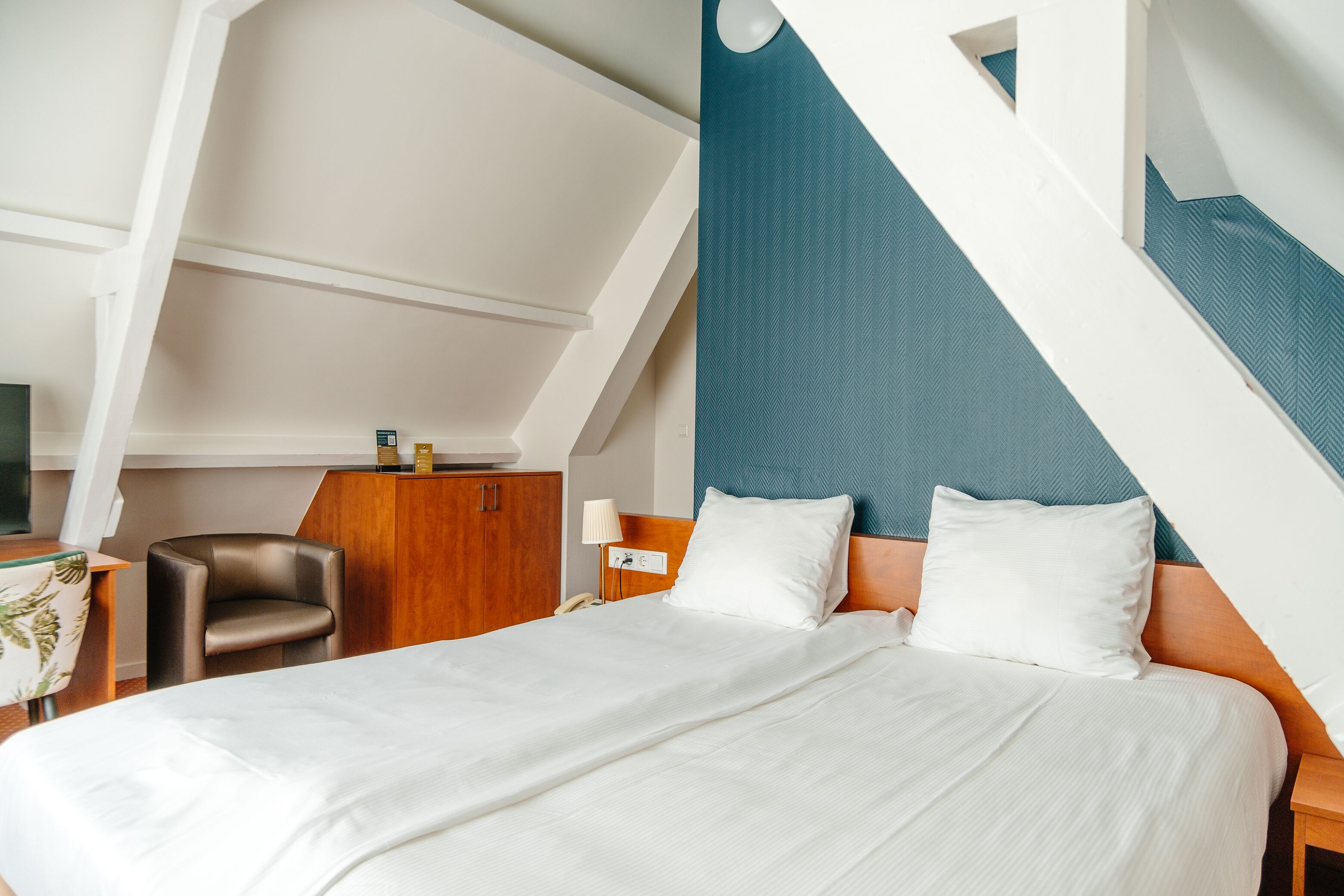 Een moderne hotelkamer met een groot bed, een houten nachtkastje, een bureau met een lamp en een stoel.