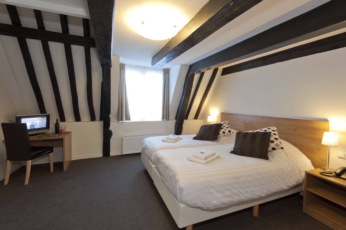 A hotel room with two beds, a desk, a chair, a lamp, and a telephone.