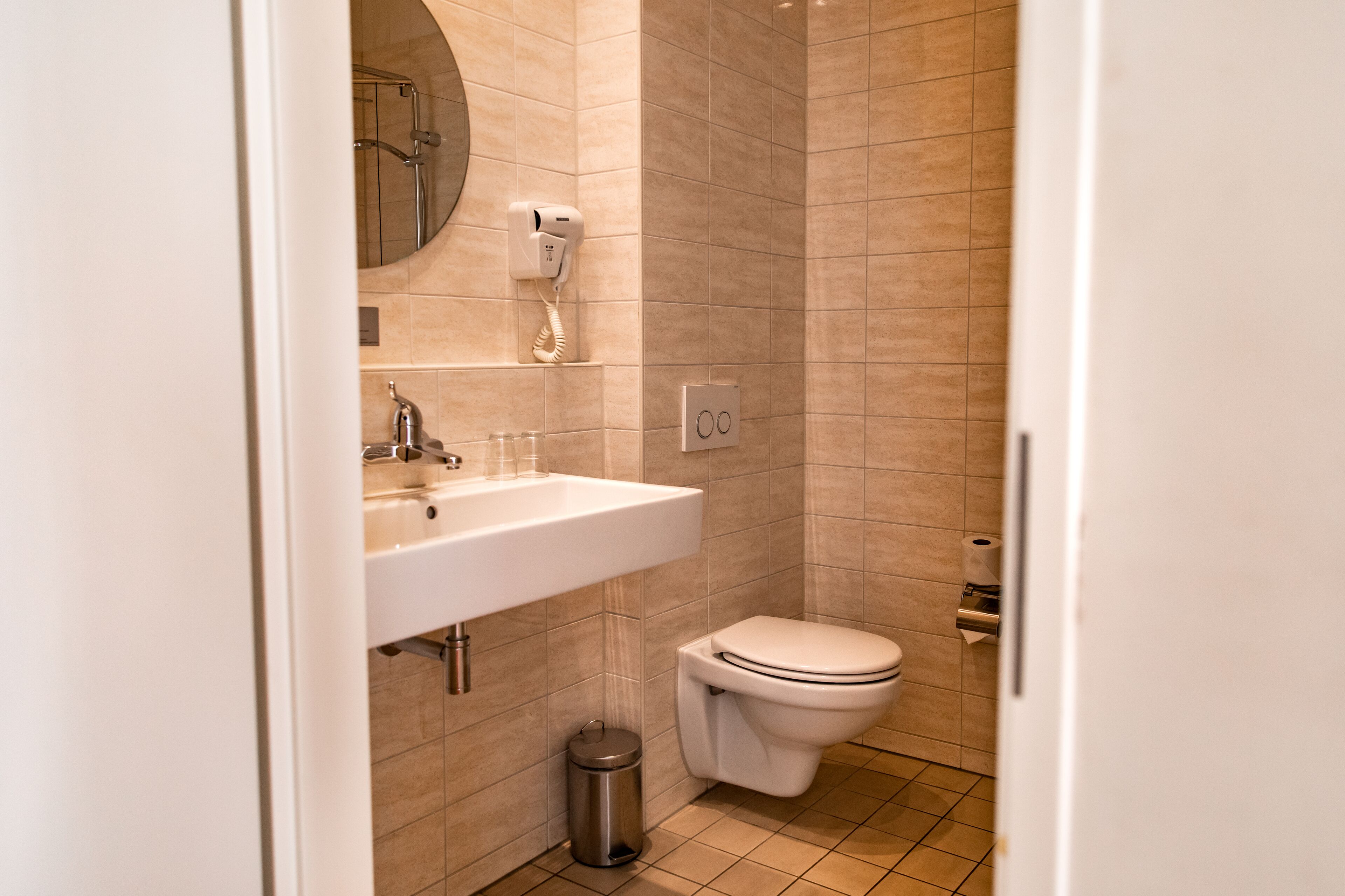 A modern bathroom with a sink, toilet, and a hairdryer mounted on the wall.
