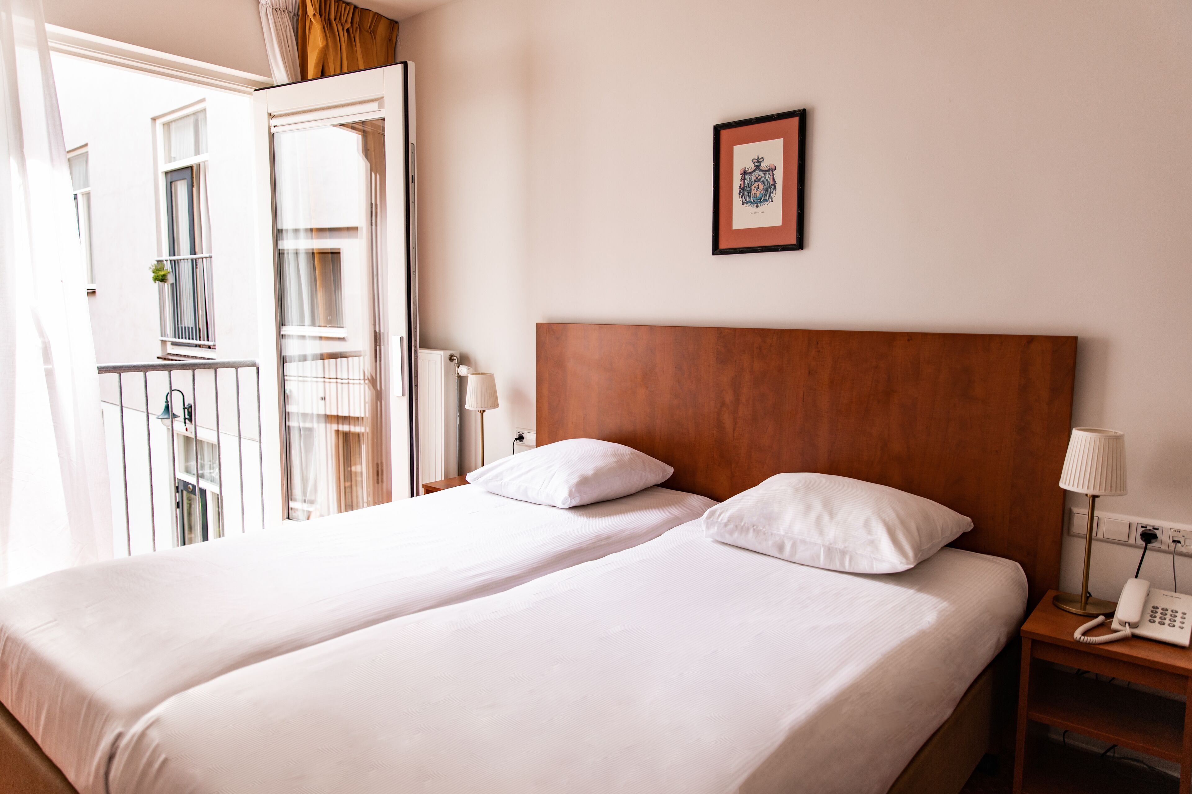 A hotel room with two beds, a wooden headboard, a bedside telephone, and a framed picture on the wall.