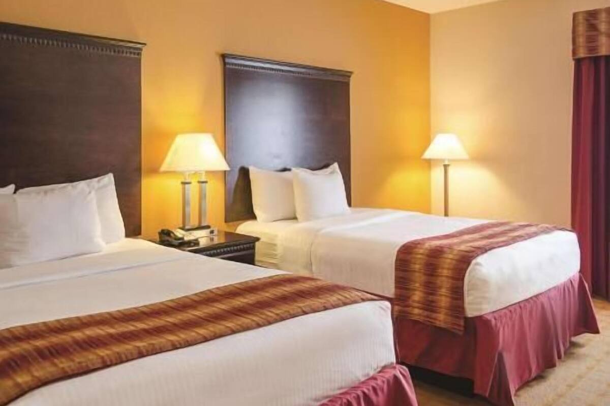 Une chambre d’hôtel avec deux lits, une tête de lit sombre, des lampes de chevet et un rideau rouge.