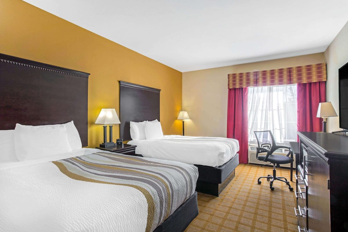 Une chambre d’hôtel avec deux lits, un bureau, une chaise et un téléviseur.