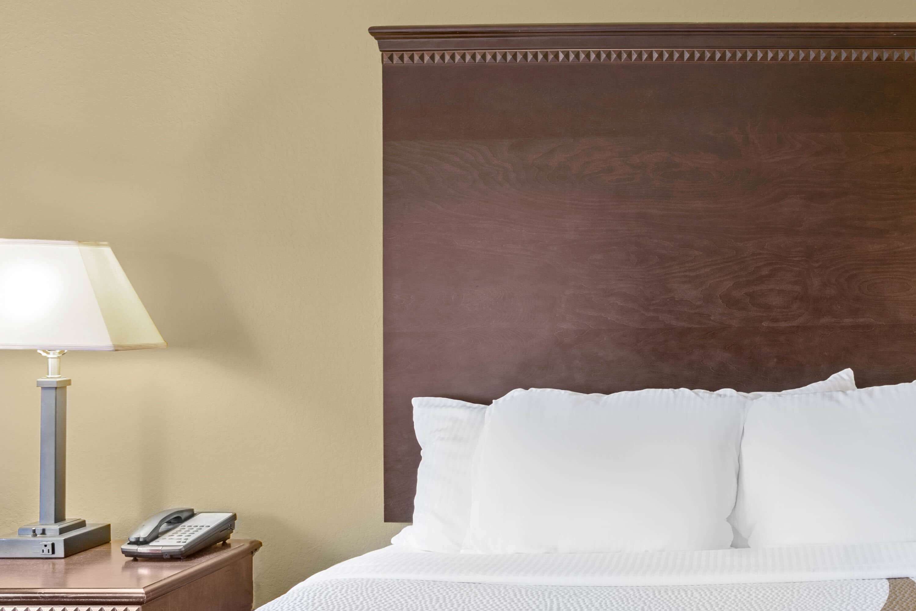 Una habitación de hotel con una cama, una lámpara de noche y un teléfono sobre una mesita de madera.