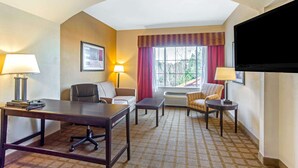 A hotel room with a conference table, two chairs, a sofa, a TV, and a window with curtains.