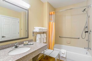 A bathroom with a sink, mirror, towel rack, shower, and a small bench.
