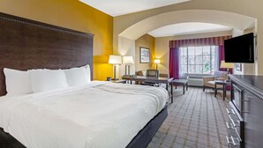 A hotel room with a large bed, a desk, a chair, a TV, and a window with curtains.