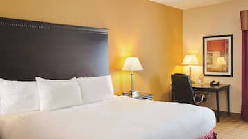 A hotel room with a large bed, two bedside lamps, a desk with a chair, and a framed picture on the wall.