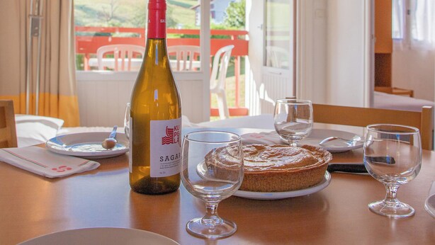 A dining table with a bottle of wine, glasses, and a plate of food. - VVF Résidence Pays Basque Saint-Jean-Pied-de-Port (Saint-Jean-Pied-de-Port)