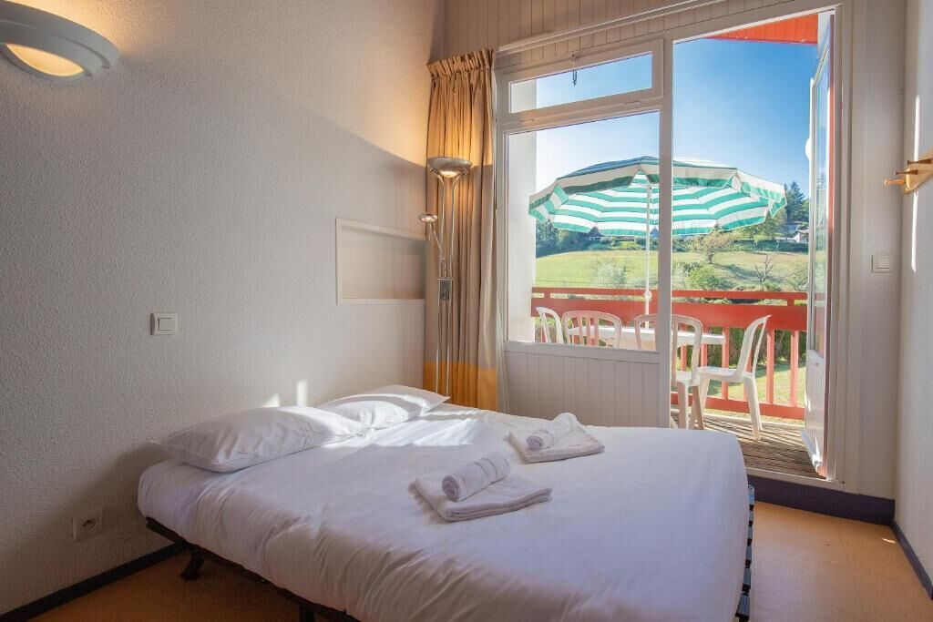 A hotel room with a bed, a window with curtains, and a view of an outdoor area with a chair and a table.