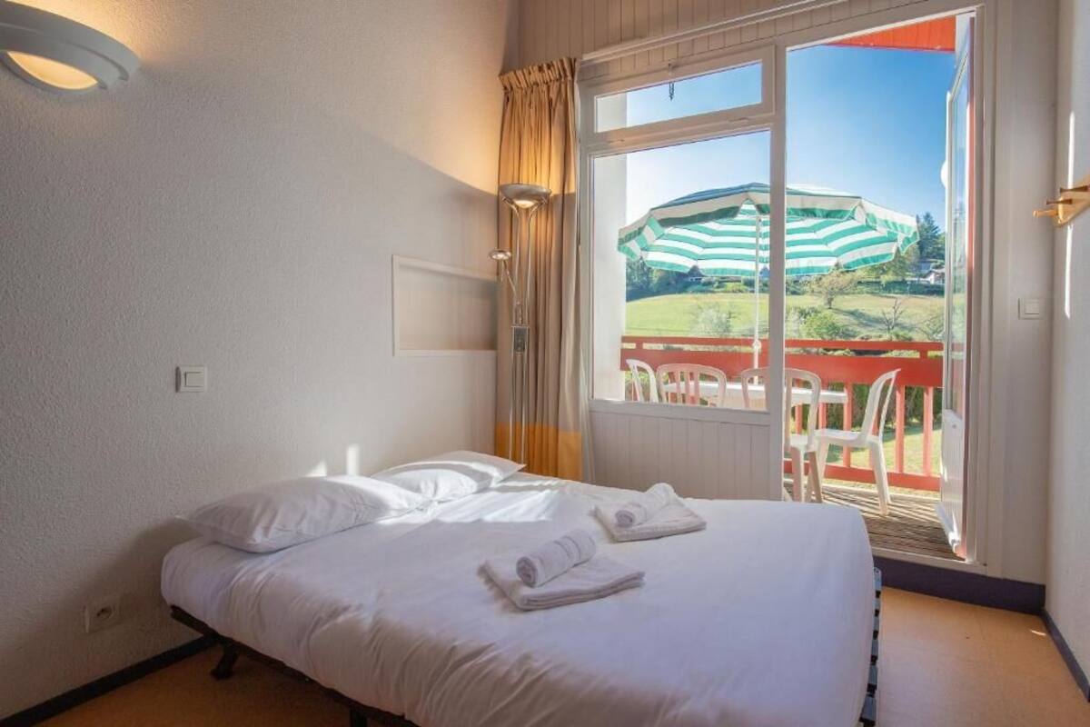 A hotel room with a bed, a window with curtains, and a view of an outdoor area with a chair and a table.