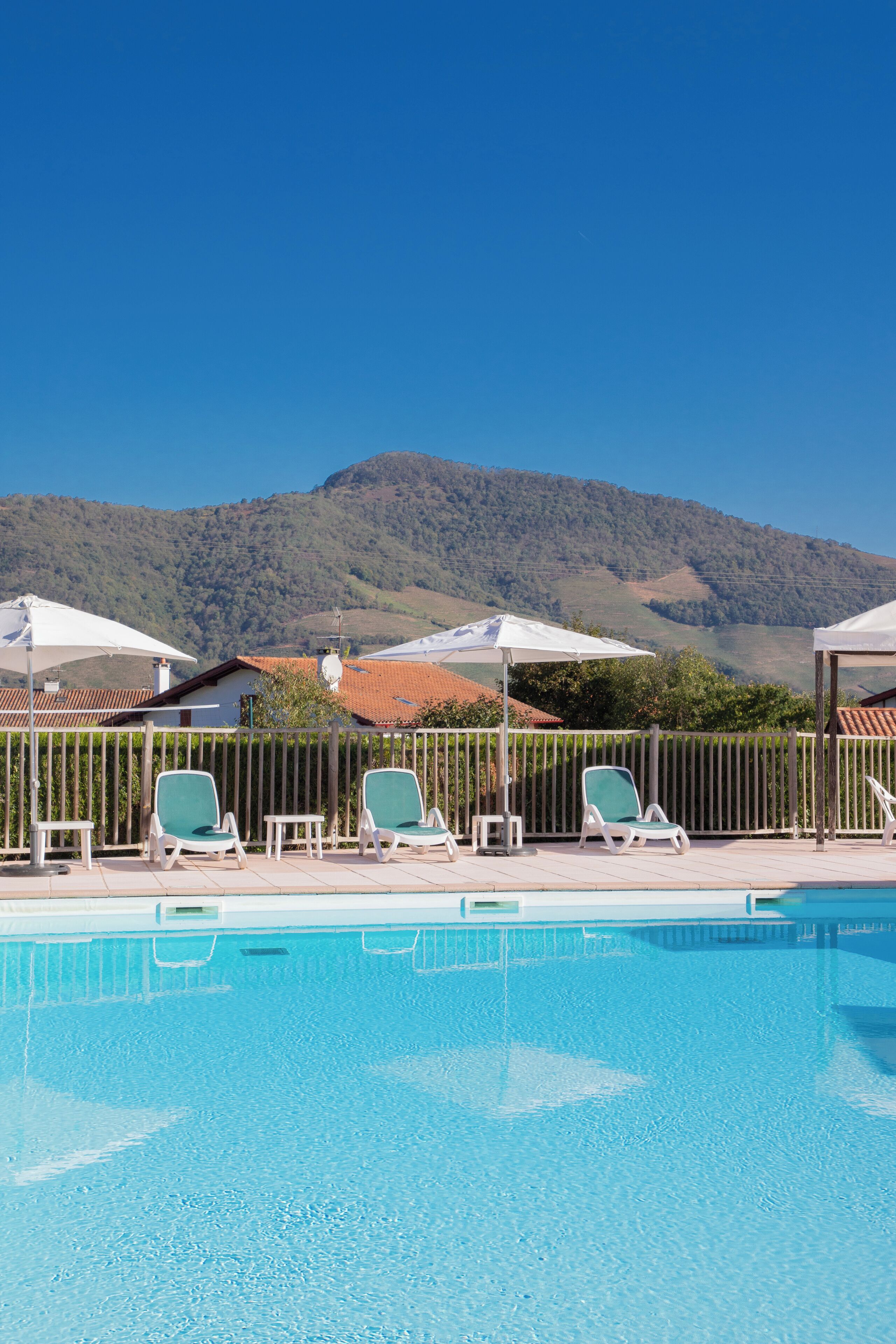 Une piscine entourée d’une clôture en bois, agrémentée de chaises longues et de parasols, avec une chaîne de montagnes en toile de fond.