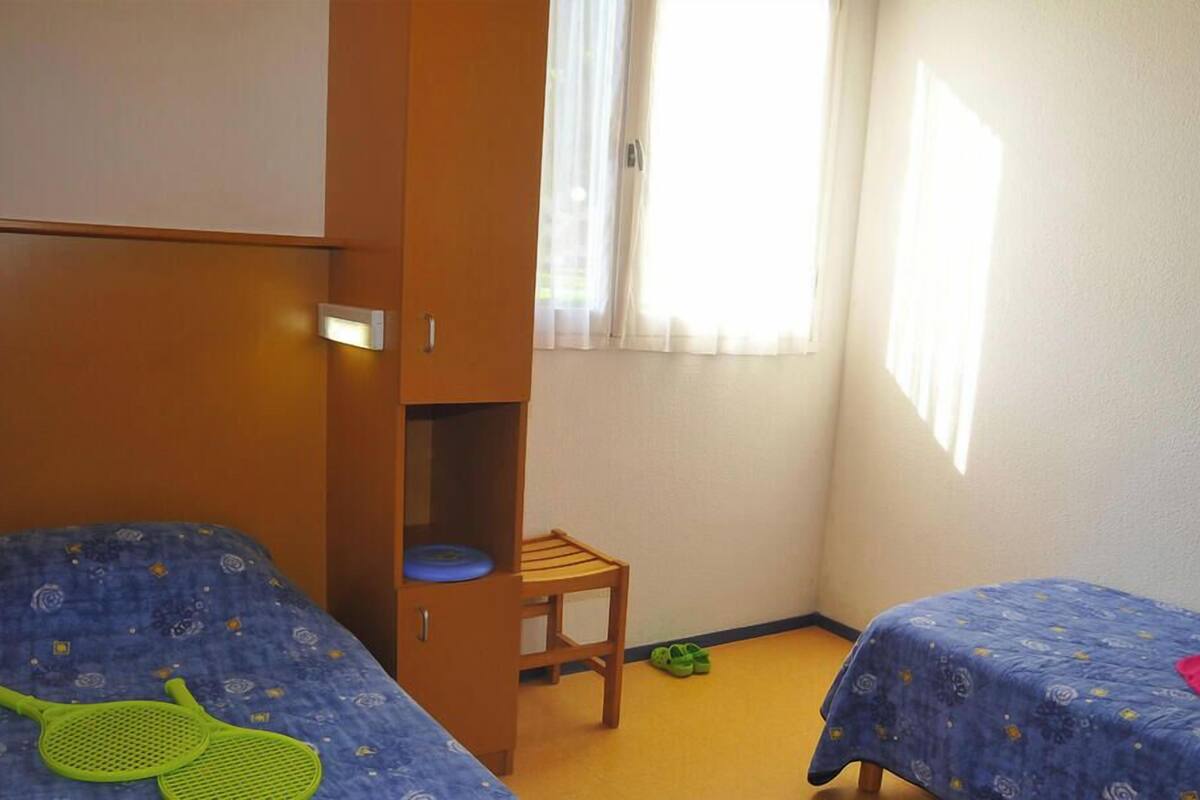 A bedroom with two beds, a wardrobe, a chair, and a window.