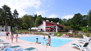 A swimming pool area with lounge chairs and a building in the background. - VVF Résidence Pays Basque Saint-Jean-Pied-de-Port (Saint-Jean-Pied-de-Port)
