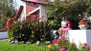 A modern building with a red roof and white walls, surrounded by lush greenery and vibrant flowers. - VVF Résidence Pays Basque Saint-Jean-Pied-de-Port (Saint-Jean-Pied-de-Port)