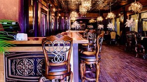 L’intérieur d’un restaurant avec des tables et des chaises en bois, des lustres et une grande plante en pot.