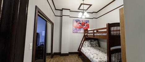 A room with a bunk bed, wooden flooring, a ceiling light fixture, and a painting on the wall.
