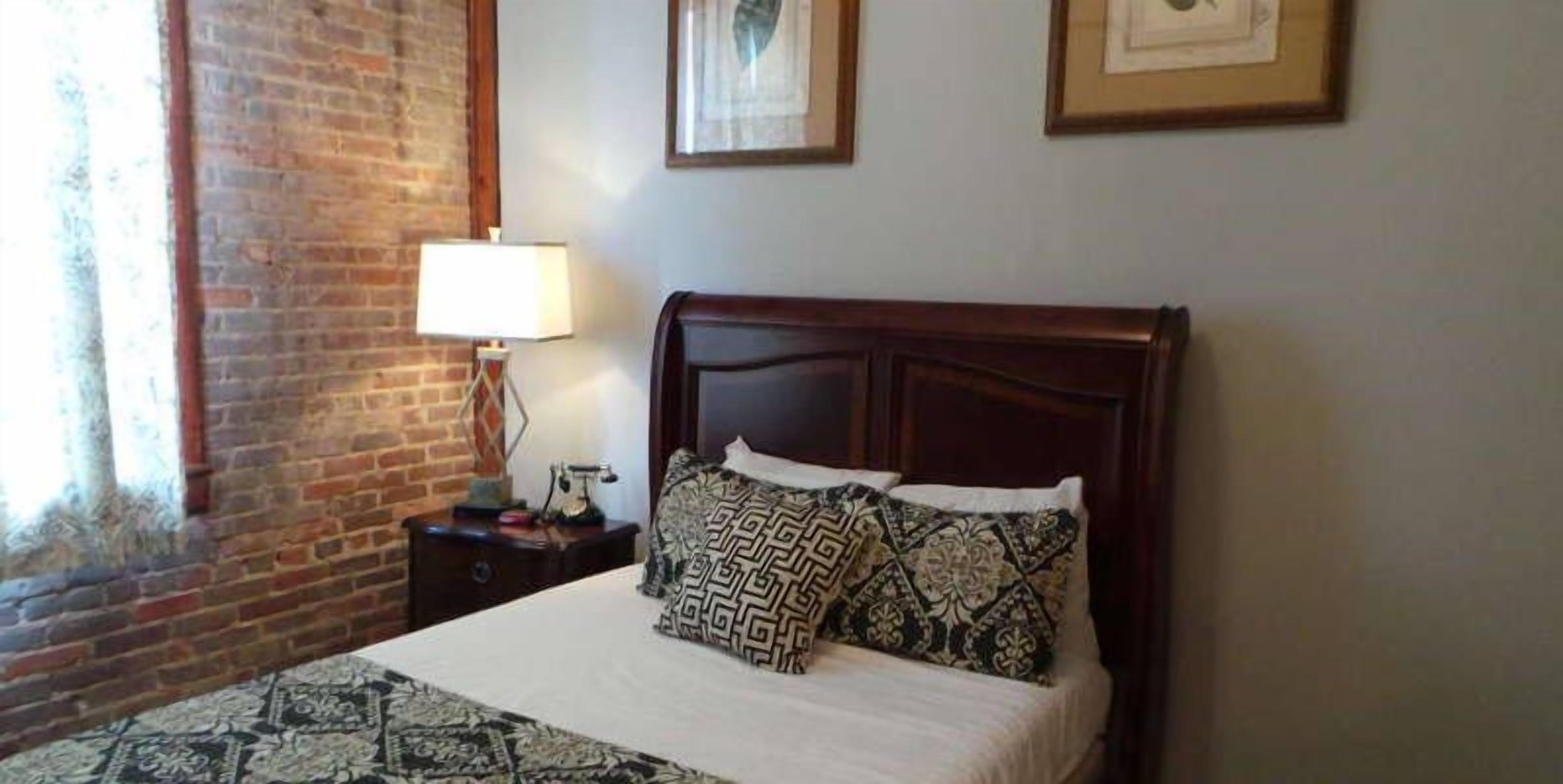 A neatly made bed with patterned pillows, a wooden headboard, and a nightstand with a lamp.